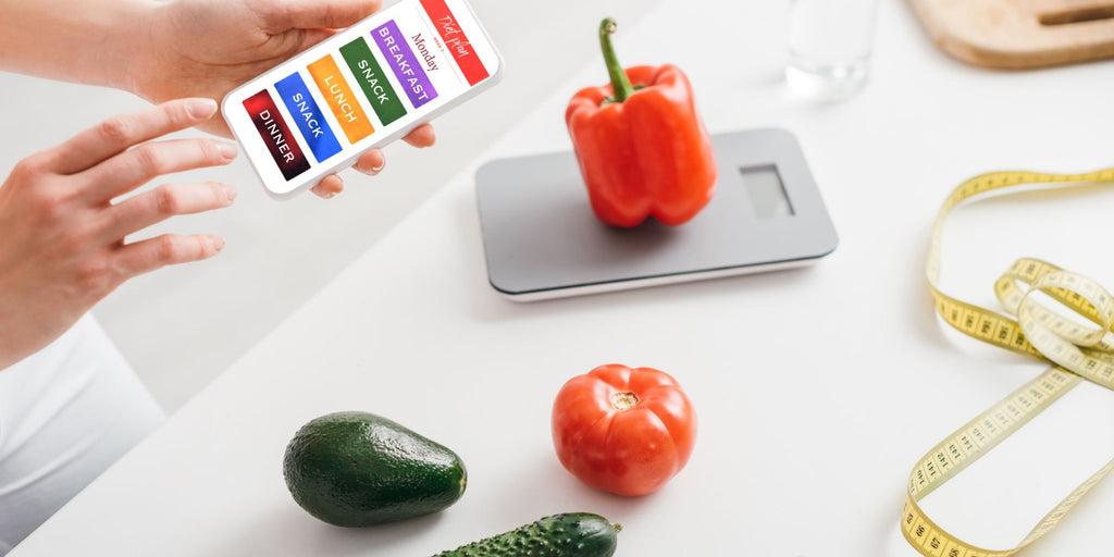 Person tracking calories on a smartphone while weighing healthy vegetables for weight loss.
