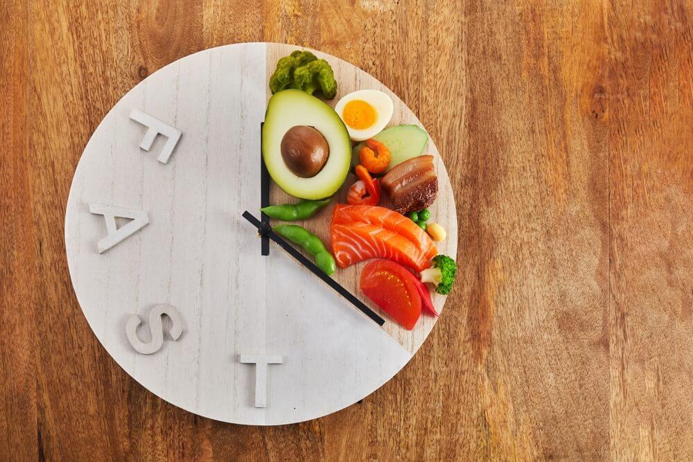 Intermittent Fasting for Weight Loss featuring a healthy balanced meal, fresh vegetables, water, and a clock representing an eating window.
